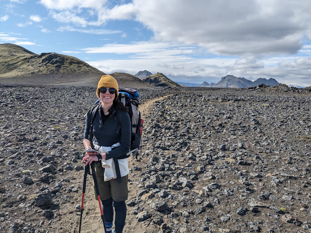 A person standing smiling to the camera with the black sand desert stretching out behind them.