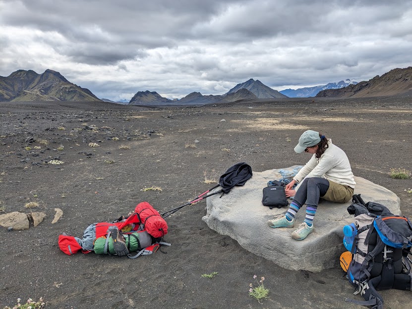 A person sitting on a big flat white rock in the black sand desert, preparing lunch.
