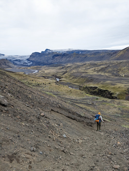 A person walking down hill towards a river canyon.