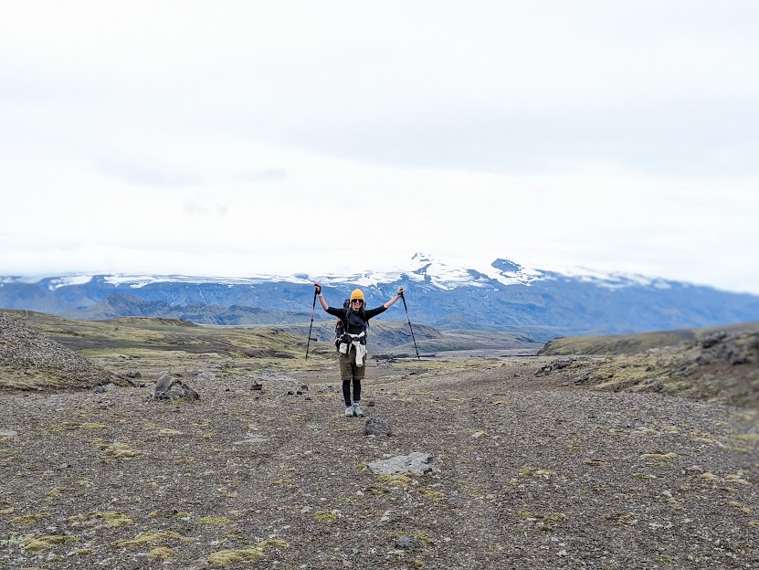 A person lifting their hands up in celebration as the valley of Þórsmörk can be seen in the background. Looming over it is the glacier Eyjafjallajökull.
