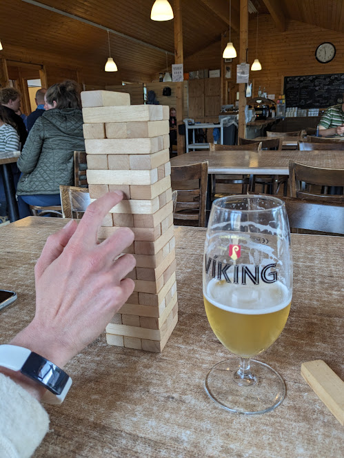 A tower of jenga cubes on a table, with a hand poking it. A half a beer can be seen next to it.